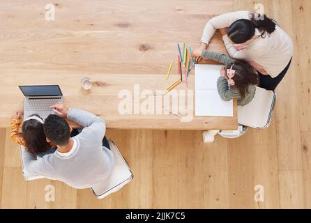 Eine Familie, die zusammen studiert, wächst zusammen. Zwei Eltern helfen ihren Kindern bei ihren Hausaufgaben. Stockfoto