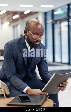 Ein seriöser Geschäftsmann aus Afrika, der in der Lobby einen Bericht liest und sich auf das Treffen vorbereitet Stockfoto