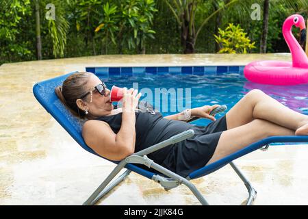 Ältere Frau, die sich in einem Liegestuhl am Pool entspannen kann Stockfoto