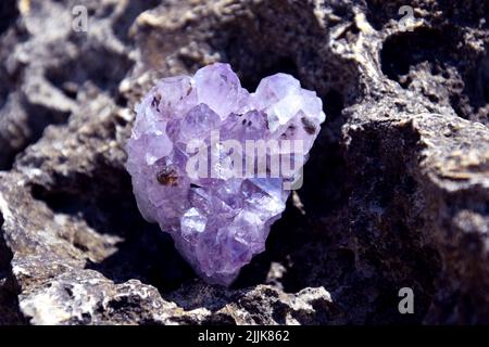 Ein schöner Amethyst drusen liegt auf einem Stein. Ein Spleiß aus violetten Kristallen aus semi-kostbarem Quarz in Form eines Herzens. Stockfoto