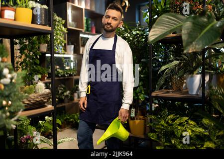 Bouquet Designer mit einer Gießkannte zum Bewässern von Pflanzen umgeben von Topfblumen Stockfoto