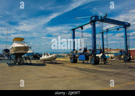 Ein fahrbarer Hängeschiff oder Hebezeug und ein kleines Freizeitboot, das auf einer Bootskradle am Yachthafen von Izola an der slowenischen Adriaküste repariert wird Stockfoto