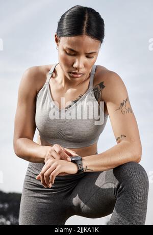 Nie war es einfacher, Ihre Fortschritte zu verfolgen. Eine sportliche junge Frau überprüft ihre Smartwatch, während sie im Freien trainiert. Stockfoto