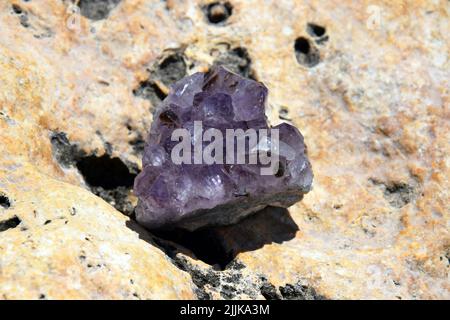 Wunderschöne violette Amethyst-Kristalle auf einem gelben Stein am Meer. Leuchtend lila Amethyst drusen in Form eines Herzens vor dem Hintergrund der se Stockfoto