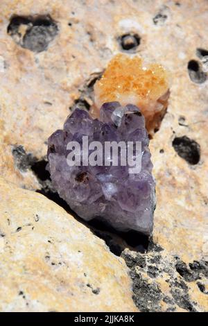 Schöne violette Kristalle aus Amethyst und Druse Cetrinum auf einem gelben Stein an der Küste. Leuchtend lila Amethyst drusen in Form eines Herzens wieder Stockfoto