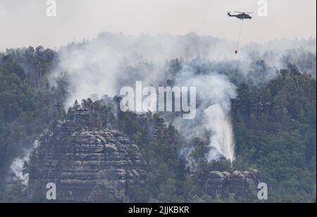 Schmilka, Deutschland. 27.. Juli 2022. Ein Hubschrauber der Bundeswehr fliegt mit einem externen Wasserbehälter, um einen Waldbrand im Nationalpark Sächsische Schweiz zu löschen. Kredit: Robert Michael/dpa/Alamy Live Nachrichten Stockfoto