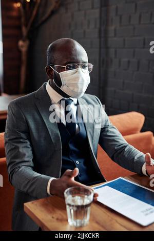 Afrikanischer Geschäftsmann in Anzug mit Schutzmaske bei einer Besprechung im Restaurant Stockfoto