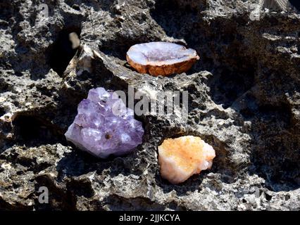 Eine schöne Druse und Geode aus Amethyst und Druse aus Citrin liegen auf einem Stein. Kristalle von Halbedelsteinen in der Sonne. Stockfoto