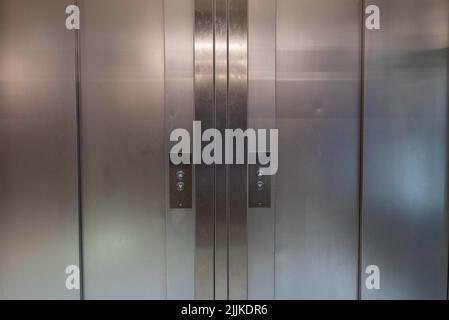 Symmetrische Aufzugstüren aus Metall mit Knöpfen zum auf- oder Absteigen. Es gibt keine Personen oder Marken in der Aufnahme. Stockfoto