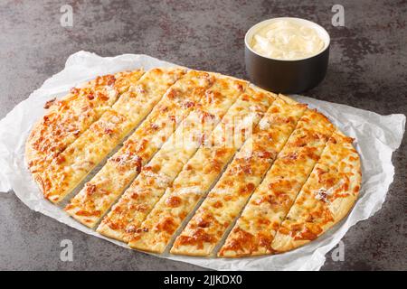 Hausgemachte Knoblauchfinger mit Mozzarella-Käse, Speck und Kräuterbutter und Donair-Sauce Nahaufnahme auf Papier auf dem Tisch. Horizontal Stockfoto