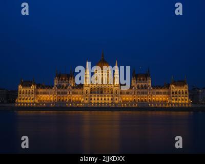 Parlamentsgebäude in Budapest, Ungarn. Parlament und Überlegungen in der Donau. Abendbeleuchtung des Gebäudes. Stockfoto