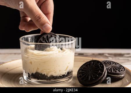 Eine Person, die mit einem Keks einen Käsekuchen in einer Glastasse schmückt. Stockfoto