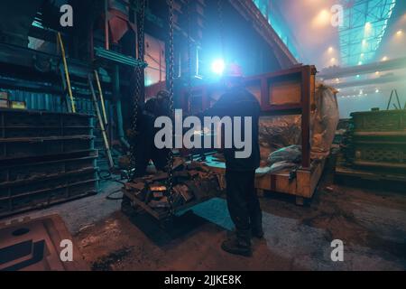 Nicht erkennbare Arbeiter in der Stahlfabrik laden Eisen. Gießerei, Metallurgie-Industrie. Stockfoto