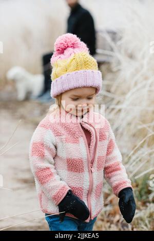 Ein Nahaufnahme-Porträt eines kleinen Mädchens in einer rosa Jacke, das auf einem Pfad geht und die Natur erkundet Stockfoto