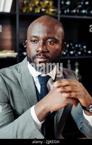 Ernsthafter afrikanischer Geschäftsmann in elegantem Anzug schaut weg, während er im Restaurant auf jemanden wartet Stockfoto