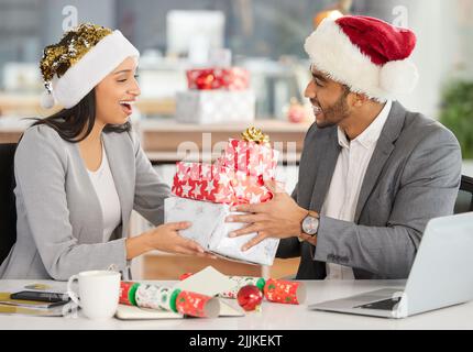 Ein junger Geschäftsmann und eine Geschäftsfrau tauschen Weihnachtsgeschenke in einem modernen Büro aus. Stockfoto