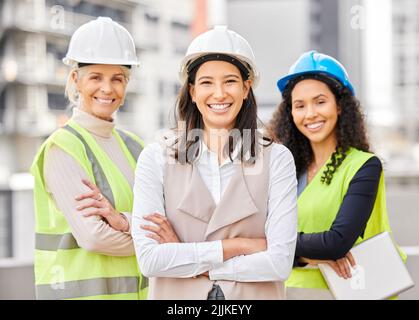 Waren die Aufgabe. Beschnittenes Porträt von drei attraktiven Ingenieurinnen, die mit gefalteten Armen auf einer Baustelle stehen. Stockfoto