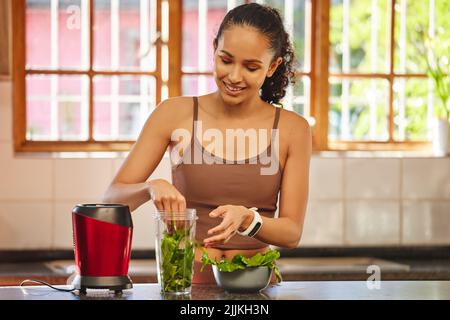 Dosierung von Eisen und Vitamin B. eine attraktive junge Frau, die allein in ihrer Küche steht und einen Frühstücksmoothie zubereitet. Stockfoto