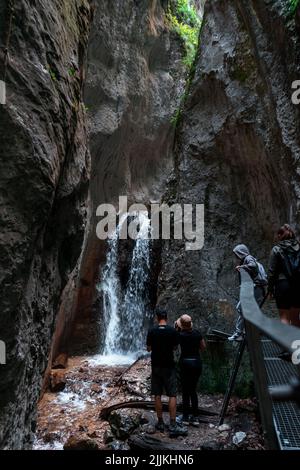 Eine vertikale Aufnahme eines kleinen Wasserfalls am Seven Ladders Canyon in Rumänien mit Touristen, die den Bach betrachten Stockfoto