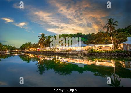 Ein Fernblick auf das wunderschöne Resort mit Gebäuden und Bäumen, die sich während des Sonnenuntergangs im Wasser spiegeln