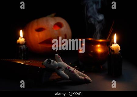 Halloween Kürbis mit brennendem Mund, Buch und einer Voodoo Puppe - Volt auf dunklem Hintergrund. Halloween-Konzept. Stockfoto