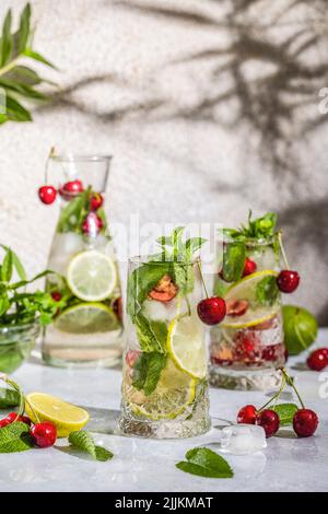 Cocktail aus Cherry Mojito in Longdrinkglas oder Mocktails, umgeben von Zutaten und Bar-Werkzeugen auf hellgrauer Tischfläche. Bereit zum Trinken. Stockfoto