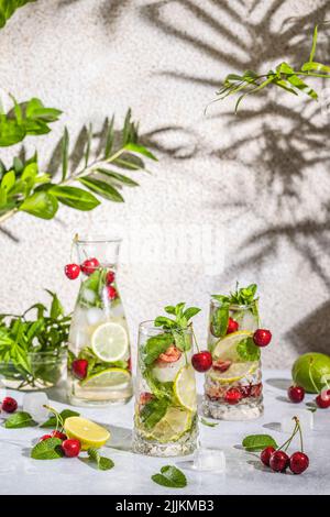 Cocktail aus Cherry Mojito in Longdrinkglas oder Mocktails, umgeben von Zutaten und Bar-Werkzeugen auf hellgrauer Tischfläche. Bereit zum Trinken. Stockfoto