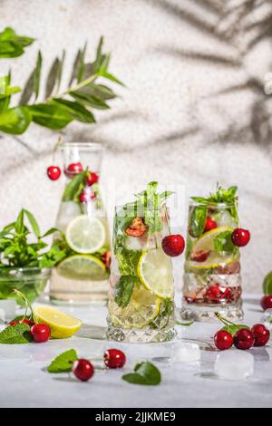 Cocktail aus Cherry Mojito in Longdrinkglas oder Mocktails, umgeben von Zutaten und Bar-Werkzeugen auf hellgrauer Tischfläche. Bereit zum Trinken. Stockfoto