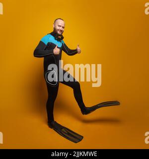 Sommerurlaub, Reisen und Seenruhe Konzept. Fröhlicher Mann mit Tauchanzug und Flossen auf gelbem Hintergrund Stockfoto