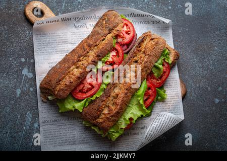 Zwei dunkle Ciabatta-Sandwiches mit grünem Salat, reifen roten Tomaten, Zwiebeln und Thunfisch Stockfoto