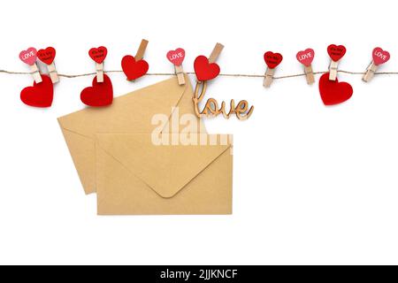 Hölzerne Wäscheklammern mit Herzen, Umschlägen und dem Wort „Liebe“, die an einer Leinenschnur hängen. Konzept für den Valentinstag. Grußkarte. Platz für Ihren Text. Stockfoto