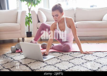 Frau trainiert zu Hause und schaut sich Videos auf dem Laptop an, sie trainiert im Wohnzimmer Stockfoto