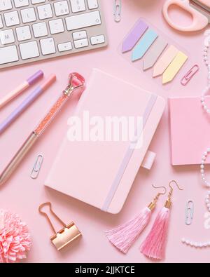 Hardcover-Notizbuch, rosa Schulzubehör und Tastatur auf hellrosa, Draufsicht, Textbuch-Modell. Girly Arbeitsplatz mit Notizbuch, Schere, Bleistift, pe Stockfoto