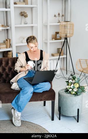 Schöne Hipster Frau in legeren Stoff mit Laptop zu Hause. Fröhliche Frau mit Laptop Stockfoto