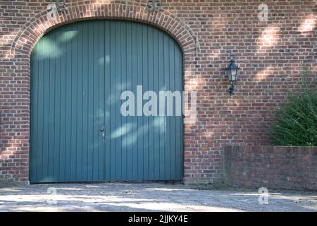 Eine große blaue Holztür in einem roten gemauerten Gebäude mit kleinen Lamopfosten an den Wänden Stockfoto