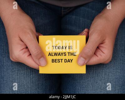 Eine Frau, die ein gelbes Papier mit dem Satz „heute ist immer der beste Tag“ in ihren Händen hält. Nahaufnahme. Stockfoto