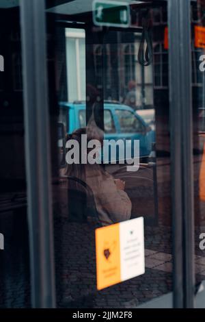 Eine vertikale Aufnahme einer Frau, die im Bus sitzt und eine blaue medizinische Gesichtsmaske trägt Stockfoto