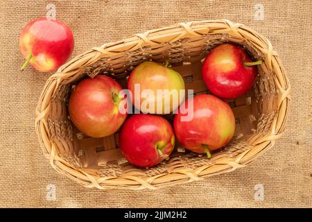 Mehrere saftige rote Äpfel in einem Korb auf Sackleinen, Makro, Draufsicht. Stockfoto