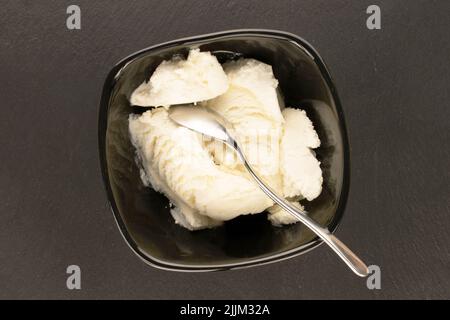Mehrere Kugeln weißes Eis in einer schwarzen Keramikschale auf einem Schieferstein, Makro, Draufsicht. Stockfoto