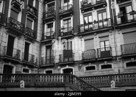 Eine Graustufenaufnahme eines Wohnhauses mit altmodischen Balkongeländern in Bilbao, Spanien Stockfoto