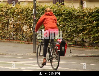 Eine Rückaufnahme eines blonden Mädchens, das in Frankfurt auf der Straße mit Bäumen auf einem Fahrrad reitet Stockfoto