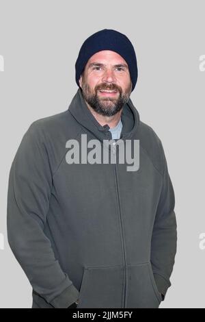 Bärtiger Mann mit blauer Beanie und grüner Kapuzenschwitze. Vorbereitung auf kühleres Herbstwetter. Stockfoto