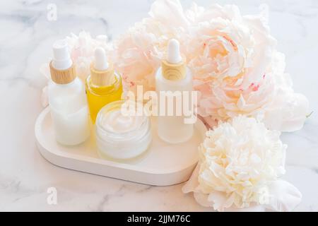 Creme, Serum, Essenz, Öl in Milchglasverpackung mit rosa Pfingstrosen-Blüten. Kosmetische Hautpflege Produkt Beton Tablett. Ausgewählter Fokus. Stockfoto