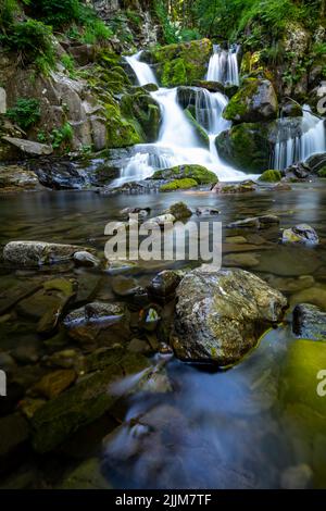 Eine vertikale Aufnahme des wunderschönen Wasserfalls, der von moosigen Felsen umgeben ist. Stockfoto
