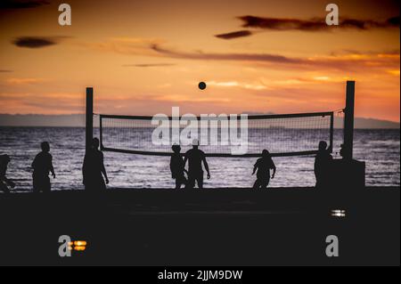 Eine schöne Aufnahme von Silhouetten von Menschen, die während des Sonnenuntergangs Volleyball spielen Stockfoto