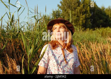 Unschärfe-Außenportrait einer schönen blonden Frau mittleren Alters in der Nähe von Schilf- und Pampagras. Jugend, Wellness und Lifestyle. 40s Frau auf Natur hintergr Stockfoto