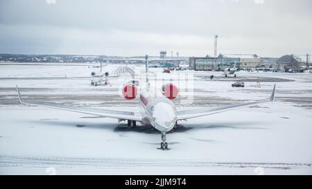 Schneebedecktes Verkehrsflugzeug am Flughafen. Nahaufnahme des Flugzeugs nach Schneefall. Flughafenmitarbeiter reinigen Start- und Landebahnen. Winter schlechte Wetterbedingungen. Stockfoto