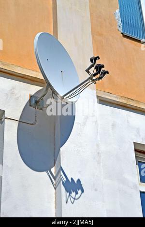 Multi-Feed-Satellitenantenne mit Mehrfachspeisung (Konverter) an der Gebäudewand mit Schatten, moderner Telekommunikationsvielfalt Stockfoto