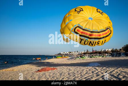 Ein gelber Fallschirm zum Parascending, der mit einem Lächeln und dem Wort „Tunesien“ geschmückt ist, ist am Strand in der Nähe von Kantaoui in Tunesien gebunden. Stockfoto