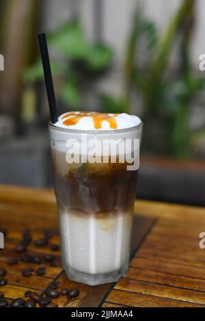 Eiskaramell-Latte mit Kaffeebohnen auf Holztisch Stockfoto